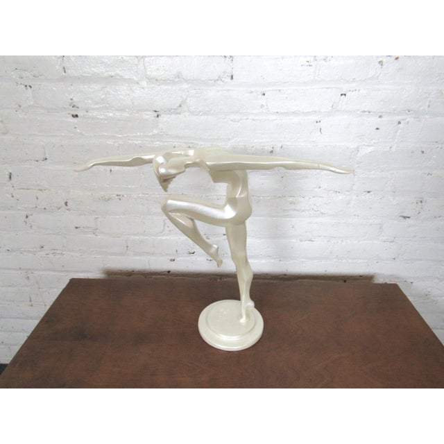 An elegant tabletop sculpture of a figure in motion. The sculpture's dynamic contours and bright white sheen can add...