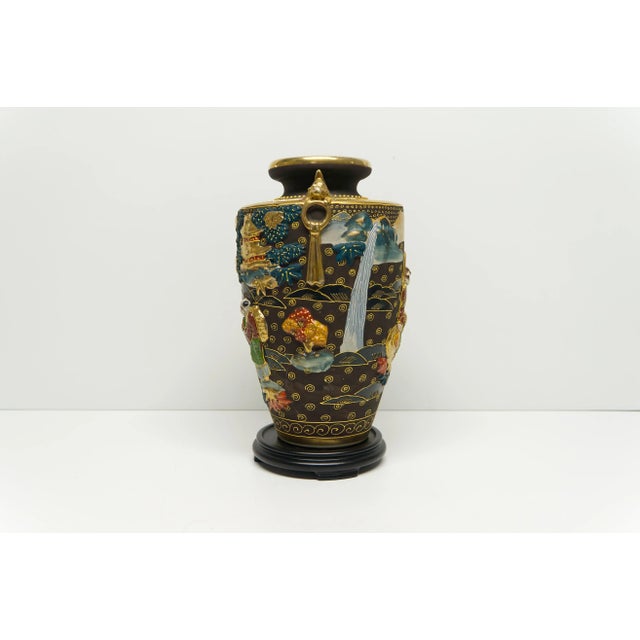 A Japanese Satsuma ceramic vase decorated in high relief and gold finish details resting on a removable wooden stand....