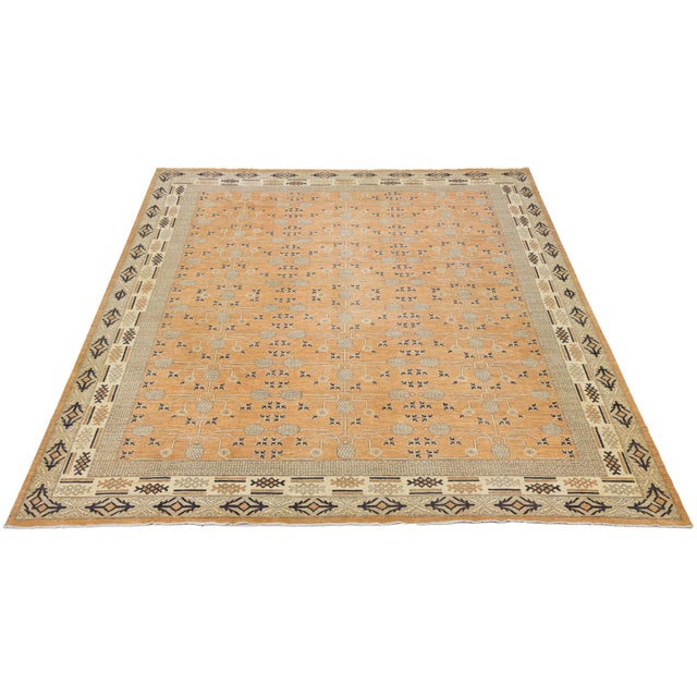 This oversized Khotan-style hand-knotted wool rug features an orange field with brown and beige accents. The design...
