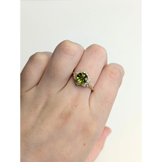 A peridot glows in a fresh olive green at the heart of this solid 14K yellow gold ring, flanked by twenty-four earth-mined...