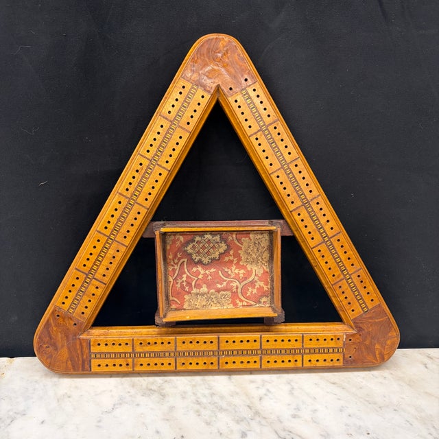Charming antique triangular cribbage board crafted with warm-toned wood and finely inlaid decorative banding. The board...