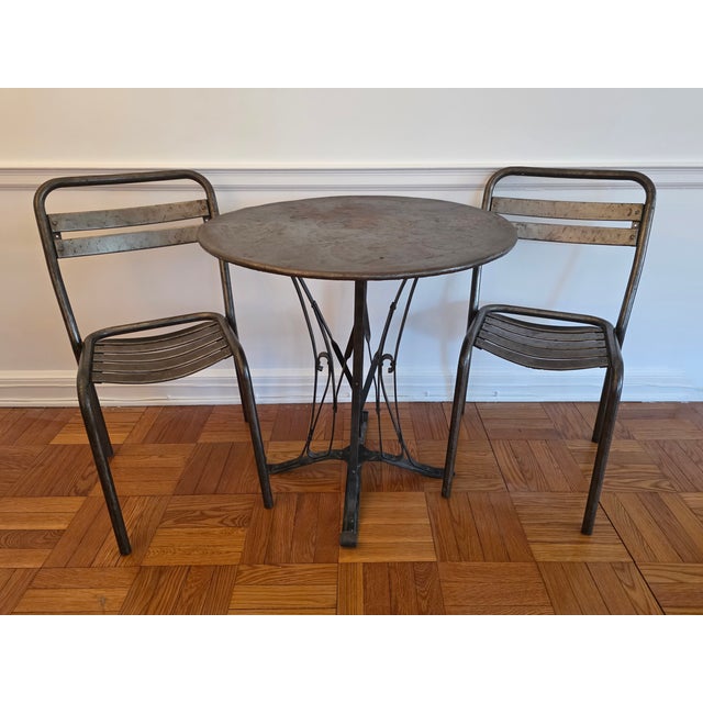 Early 20th century French Steel Bistro set with a round table and two chairs. The 26.5" diameter table has a scrolled base...