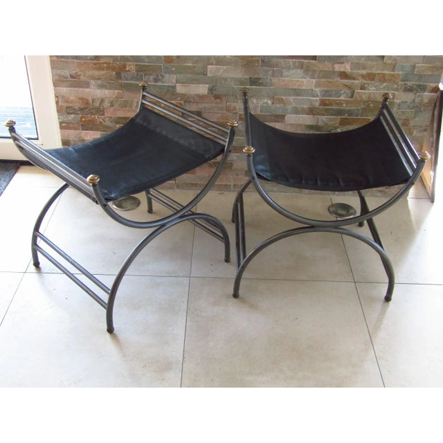 This pair of Italian stools in Empire style features patinated metal frames, leather seats, and brass details.
