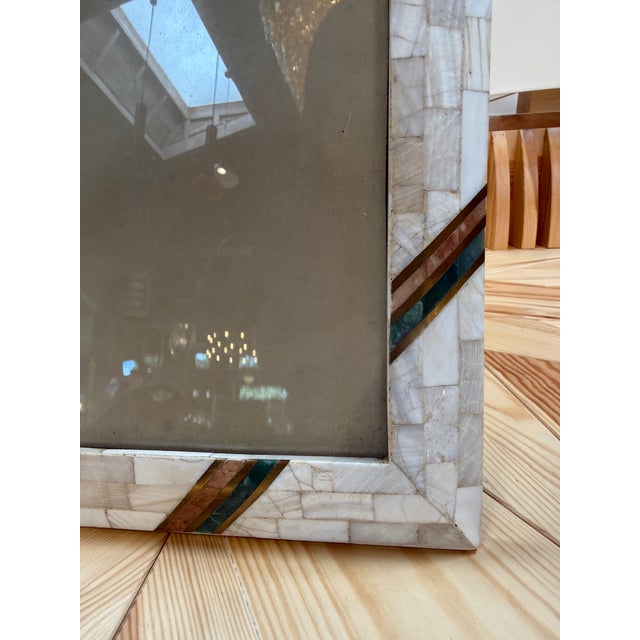 A rectangular picture frame with a mosaic of pale, subtly varied tiles. Curved brown and turquoise accents add color at...