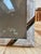 A rectangular picture frame with a mosaic of pale, subtly varied tiles. Curved brown and turquoise accents add color at...