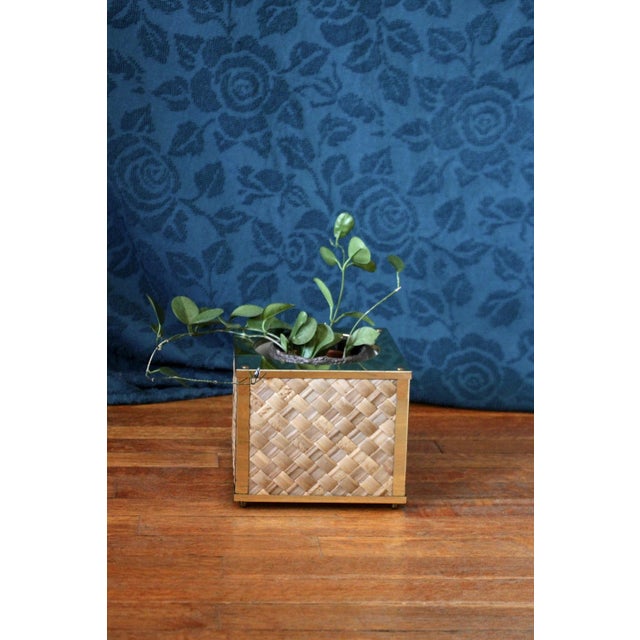 A cube planter on feet with a reed or grass criss-cross design weave in panels. Framed in shiny gold brass this has a...