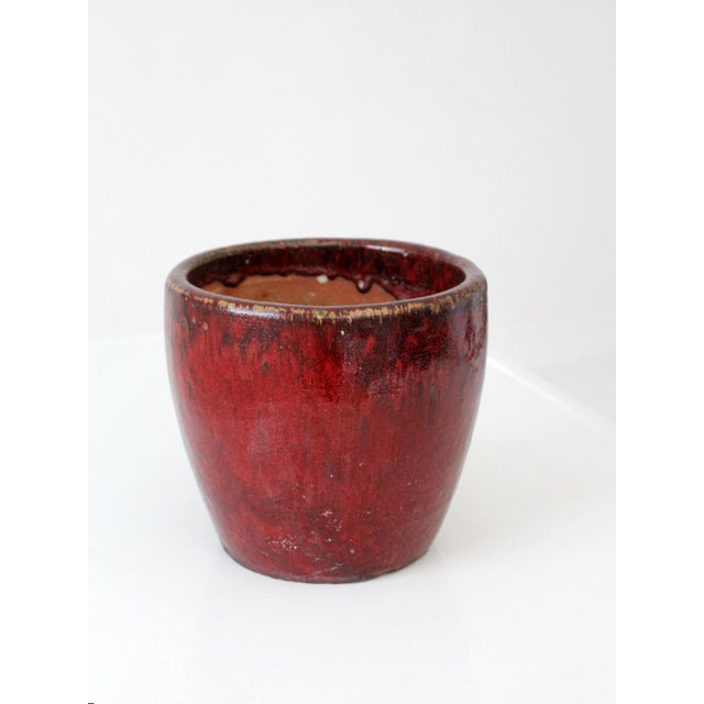 A vintage studio pottery planter with a rich oxblood glaze that shifts from deep red to near black at the rim. The softly...