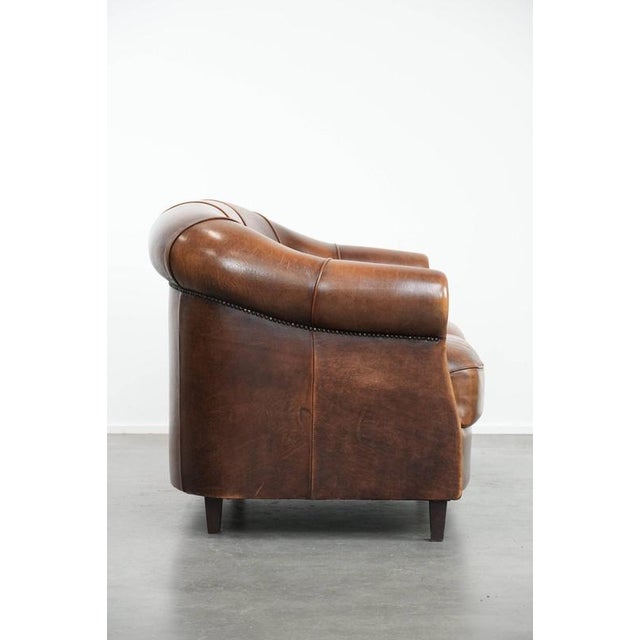 A characterful, sturdy, vintage 2-seater club sofa made of sheepskin leather with decorative studs and warm colors. : This...