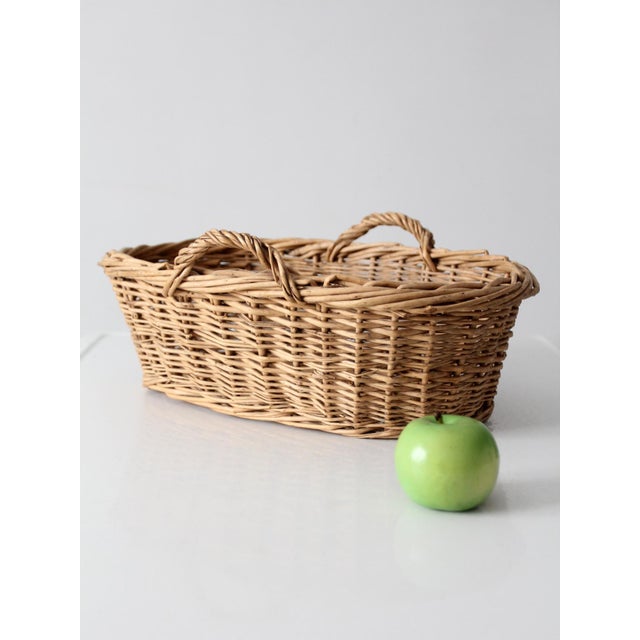 This vintage wicker basket features an elongated oval form with twisted side handles and a warm natural tone throughout....