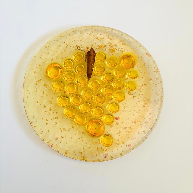 A mid century circular yellow lucite trivet with a design of grapes in the center. Smooth surface with a textured back to...