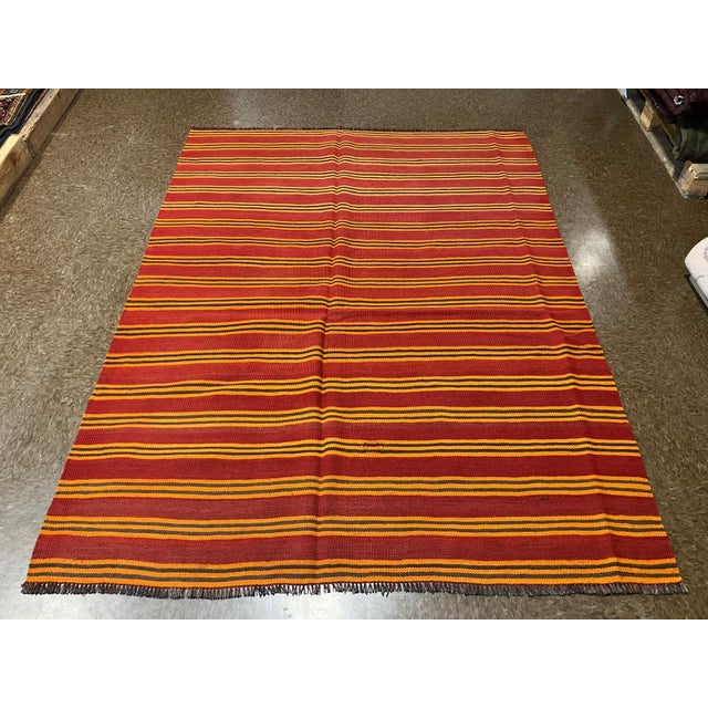 Handwoven Persian kilim flatweave rug featuring a simple striped field with alternating horizontal bands in warm tones....