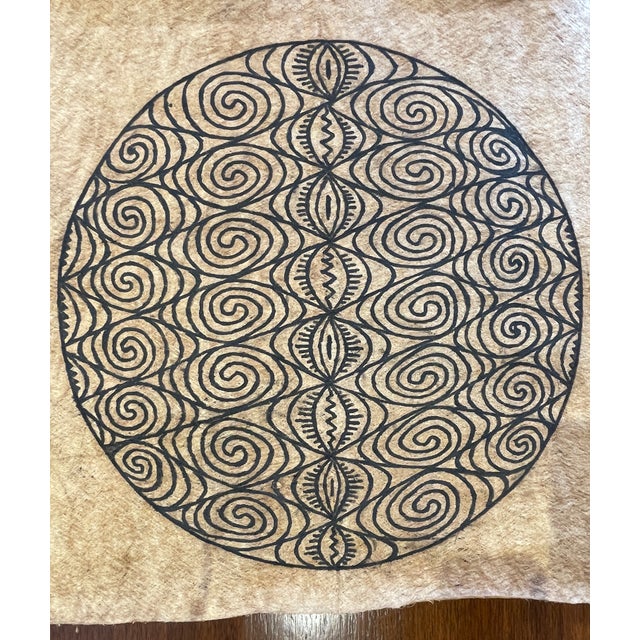 This piece features a striking symmetrical design, with circular, spiral, and diamond motifs carefully hand-drawn in black...