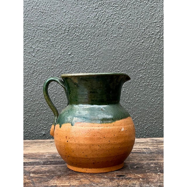 This charming vintage studio pottery pitcher exemplifies the soulful beauty of handmade functional art. Featuring a deep,...