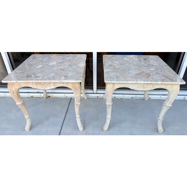 Pair of French Provincial-style tables, featuring marble tops and carved, distressed-finish wooden legs. The tables are...