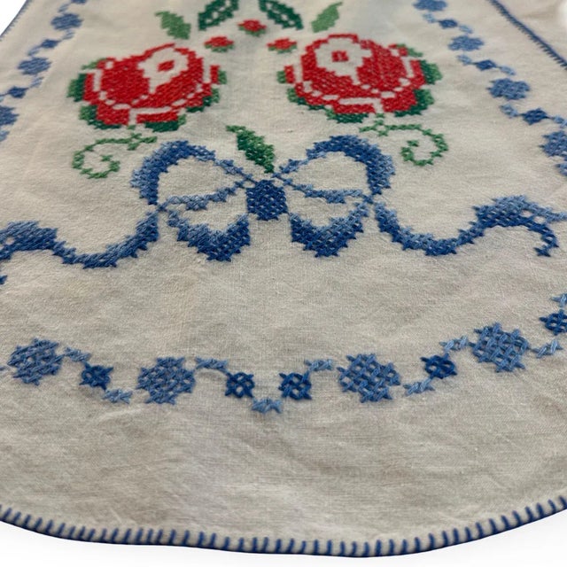 "A darling vintage apron, hand-embroidered with bright red roses, blue bows, and a full border of tiny cross-stitches....