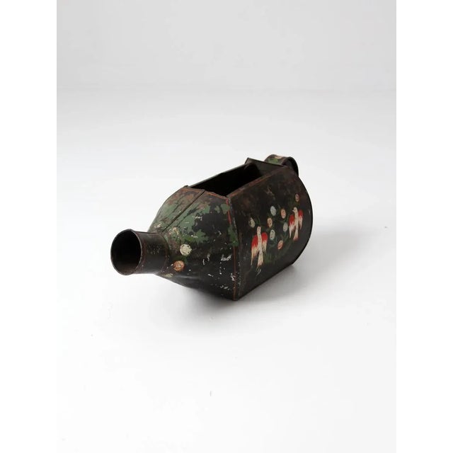 A vintage European watering can circa 1940. The black folk art tin features an elongated body, wide spout, and handle....