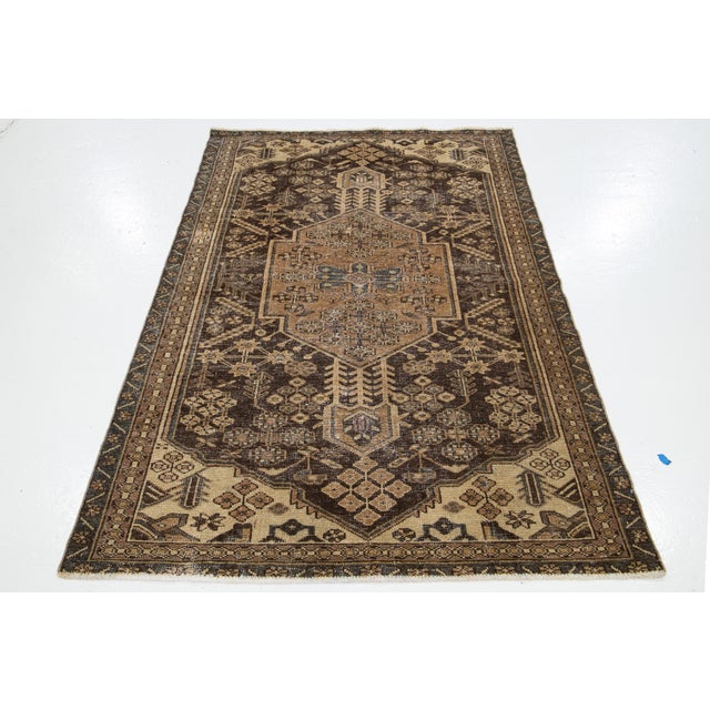Vintage Handmade distressed hand-knotted wool rug with a brownfield and beige accents in an all-over design. This rug...