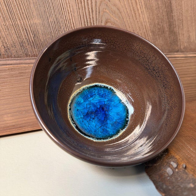 This compact matcha bowl is finished in a deep brown to near-black glaze with a pronounced, fine crackle pattern....