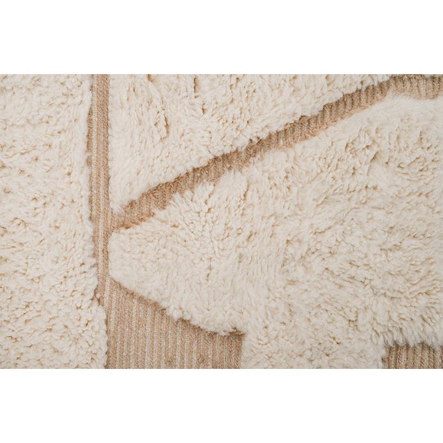 Natural hand-knotted wool rug in soft Ivory with geometric Beige accents. The raised patterns and neutral tones create a...