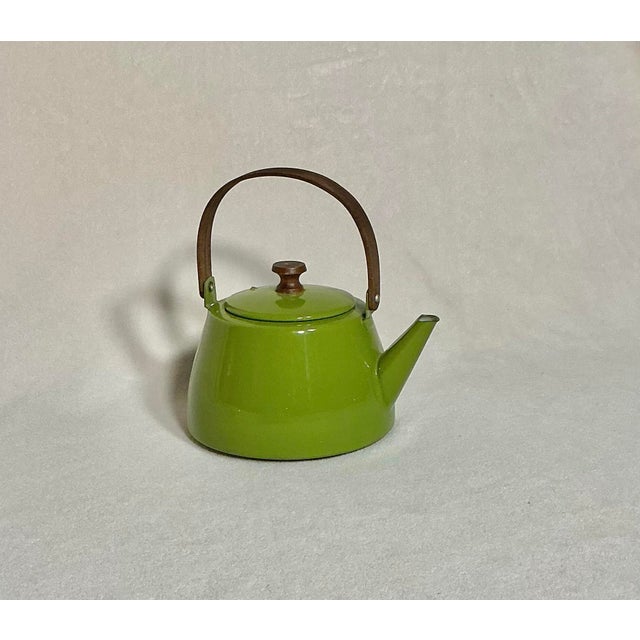 A charming vintage Mid-Century form enamel teapot in a vibrant, glossy chartreuse/avocado green finish with a natural wood...