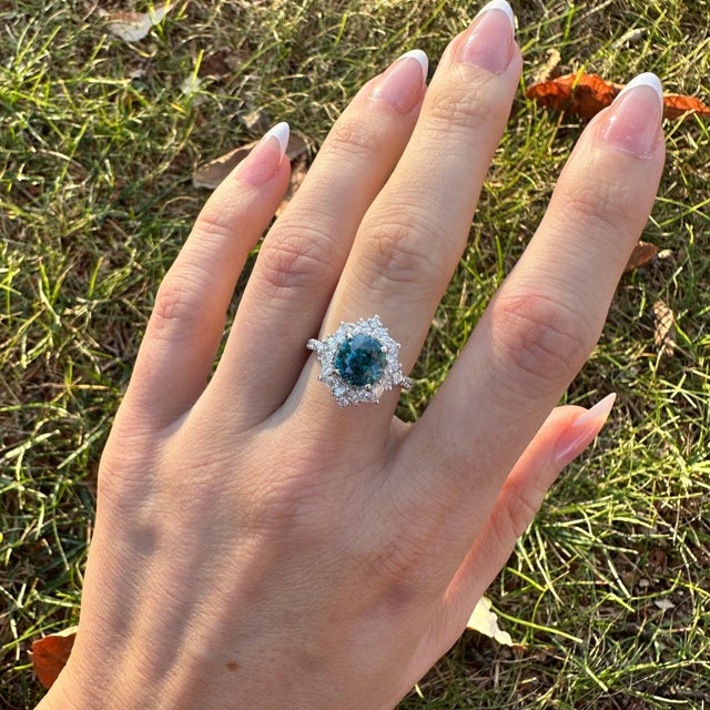 A blue zircon rests in a brilliant electric blue at the heart of this solid 14K white gold ring, flanked by thirty-four...