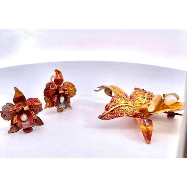 A vintage-style jewelry set featuring a large lily-shaped brooch flanked by a matching pair of screw-back earrings. The...