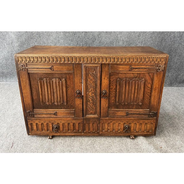 This antique carved oak buffet features richly figured wood, decorative floral carving, fluted panel details, and...