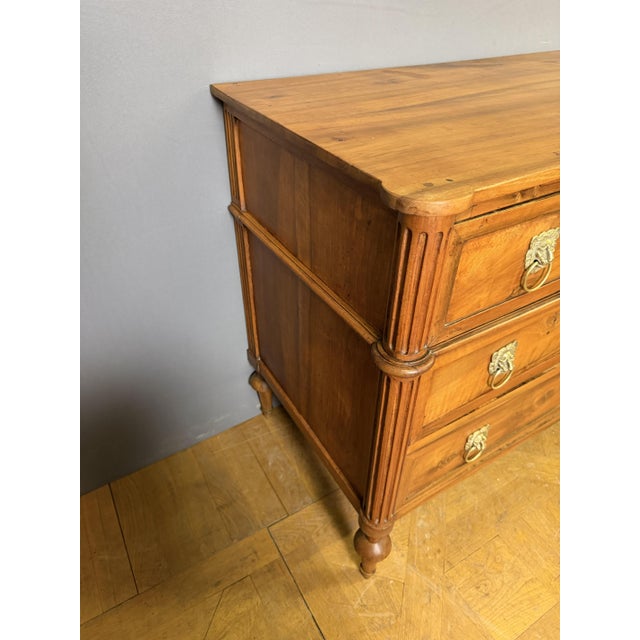 An 18th-century Louis XVI commode in light walnut. It features three drawers in the front, separated by crossbars, and...