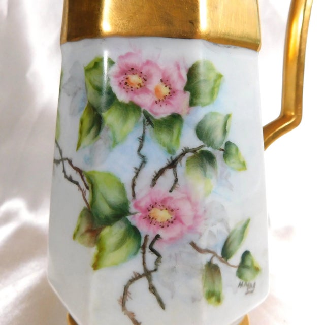 This is an unmarked white pitcher with gold trim and a floral design that is signed on one side. The pitcher measures 7.00...
