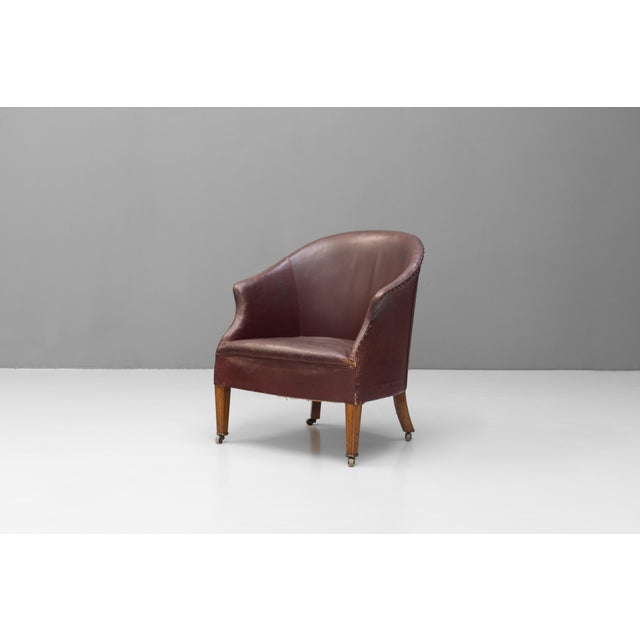 Tub chair on tapered legs in original worn burgundy leather. Circa 1920.