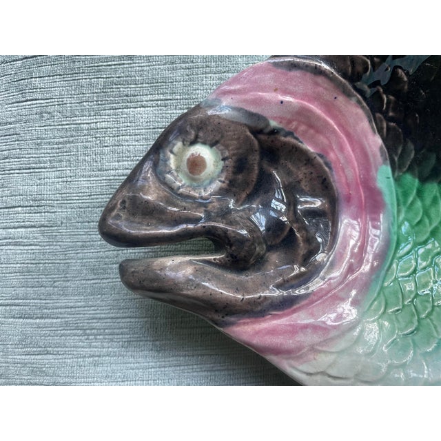 A beautiful majolica fish plate/bowl is glazed in pinks and aquas with a grey face and upper body. This piece is more bowl...