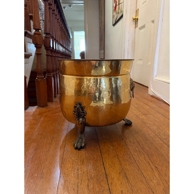 An antique hammered brass cauldron planter with three clawed feet and lion head accents. H: 12.5” D: 12.5” Depth: 10”