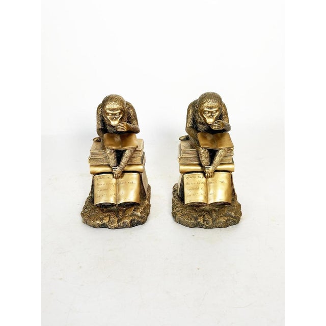 Pair of vintage gold-tone metal bookends depicting two pensive monkeys seated atop stacks of open books. Each figure...