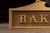 Large hand-crafted wooden storefront sign featuring raised block letters reading BAKERY across a shaped gilt panel. Each...