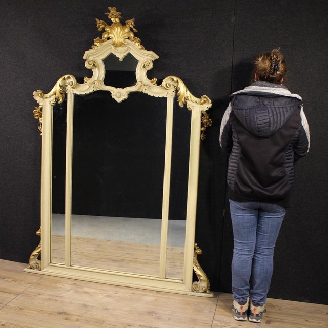 Great Italian mirror from the first half of the 20th century. A richly carved, lacquered, and gilded wooden furniture in...