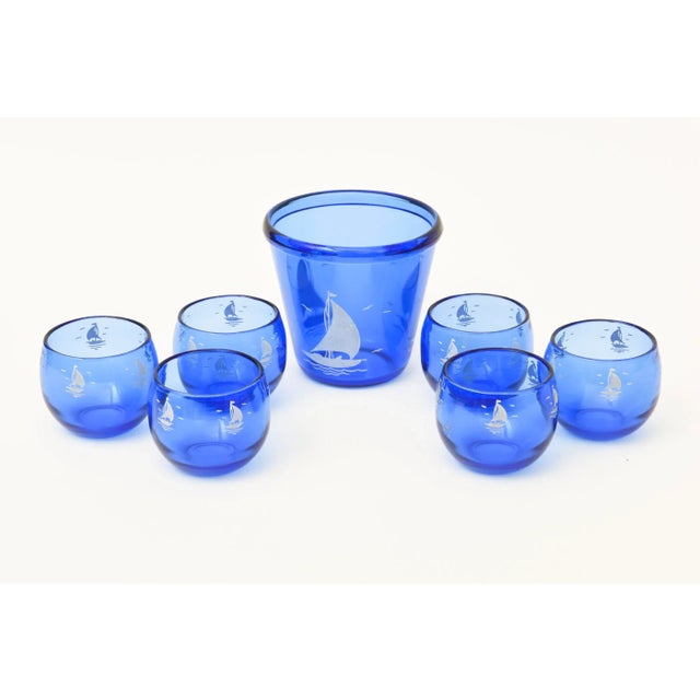 This vintage glass ice bucket and six round small cordial glasses is blue with a sailboat. We do not know if this is...