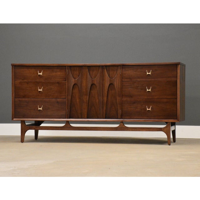 A mid century modern walnut dresser made by Broyhill Brasilia with swooping sculpted door pulls and matching polished...