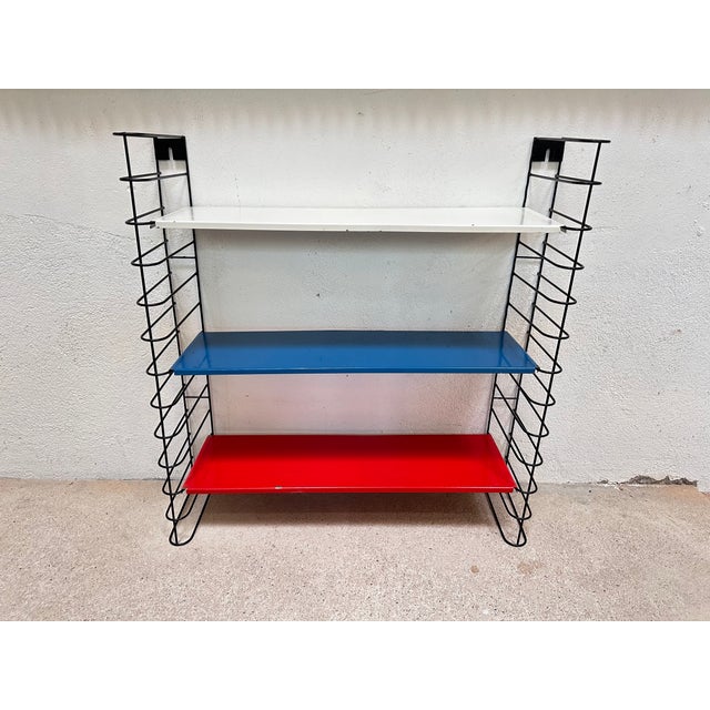 Original 1960s wall shelf with a delicate black wire frame and three removable metal shelves in white, blue, and red. The...
