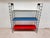 Original 1960s wall shelf with a delicate black wire frame and three removable metal shelves in white, blue, and red. The...