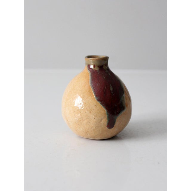 A vintage handmade studio pottery vase featuring a rounded, organic form and a softly layered glaze in warm tan with deep...
