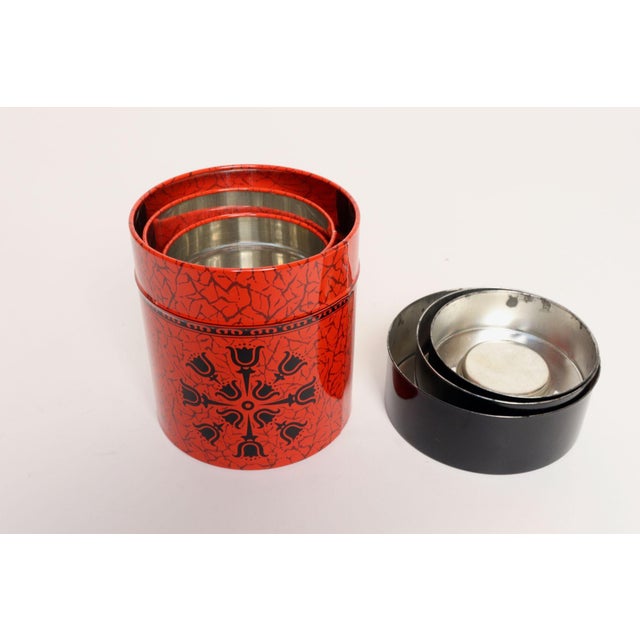 Set of three metal nesting canisters with red craclequer-style litho exterior and black floral snowflake motif (ca. 1960s,...