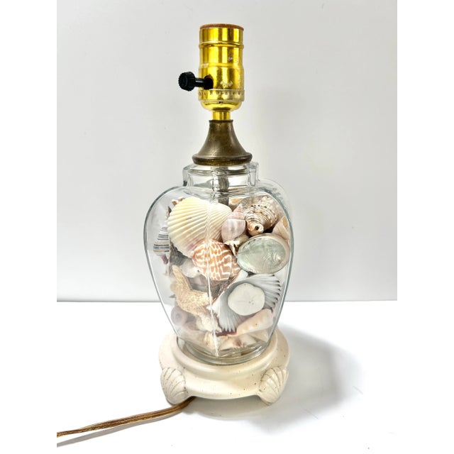 A charming 1980s coastal glass table lamp filled with an assortment of natural seashells. The clear glass body allows the...