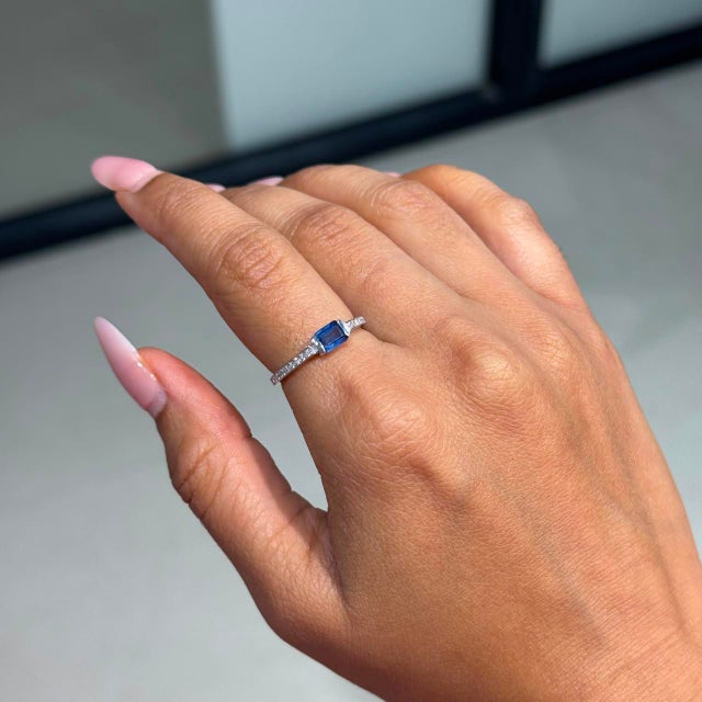 This Solitaire Ring showcases a 0.56 carat natural emerald-cut blue sapphire, set in 14k white gold. The sapphire...