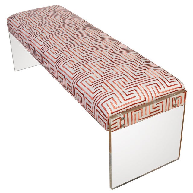 A modern bench with lucite panel supports for each side and a fully upholstered seat in a vibrant, greek key geometric...