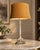 Table lamp with a tall fluted silver-tone column on an ornate base with classical details, paired with a warm brown fabric...
