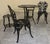 A decorative five-piece garden set featuring two chairs, a round bistro table, and a pair of matching plant stands. Raised...