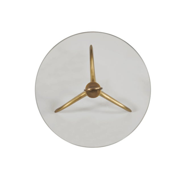 The Wilton Accent Table is crafted in brass finished metal with a singular post that pierces the clear glass top and ends...