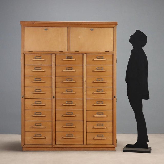 This 1950s wooden filing cabinet features a solid, linear structure typical of period design. Featuring numerous drawers,...