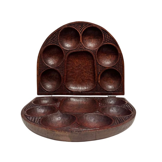A beautifully hand-carved folding wooden Mancala-style game board featuring expressive figural relief carvings on the...