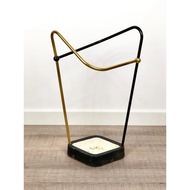 This original vintage Bauhaus style umbrella stand was produced in the 1950s in Germany. The brass colored top elements is...